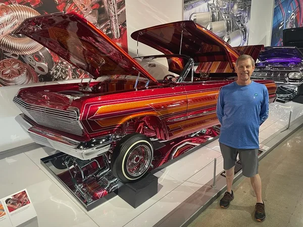 Tim D. Binegar standing beside a red custom classic car on display
