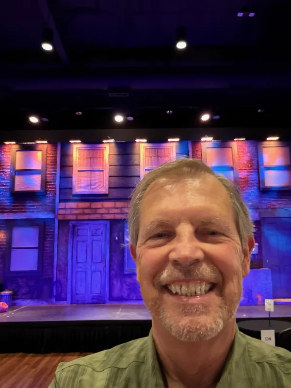 Tim D. Binegar smiling in front of a lit stage set